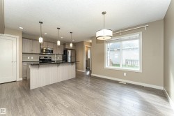 Open-concept living space featuring wood-finish flooring, a kitchen island with pendant lighting, stainless steel appliances, and a window with blinds - 
