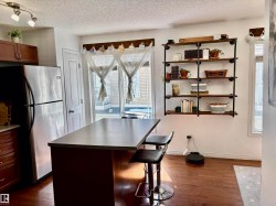 Kitchen area featuring an island with seating, stainless steel refrigerator, dark wood-finish flooring, and open shelving with metal pipe supports - 