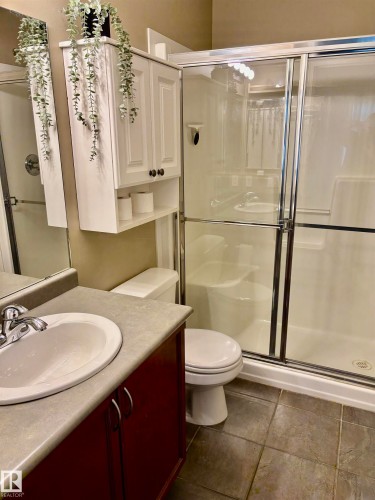 Three-piece bathroom featuring a shower with sliding glass doors, a vanity with a white basin and dark red cabinetry, and a wall-mounted storage cabinet - 184 1804 70 Street, Edmonton, AB 
