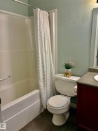 Bathroom featuring a white tub/shower combination with a grab bar, a white toilet, a vanity with a dark countertop, and tile flooring - 