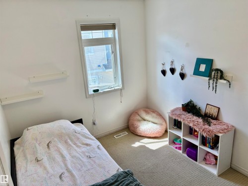 Bright room featuring a window with a roller shade, light-colored carpeting, white baseboards, and multiple white wall-mounted shelves - 184 1804 70 Street, Edmonton, AB 