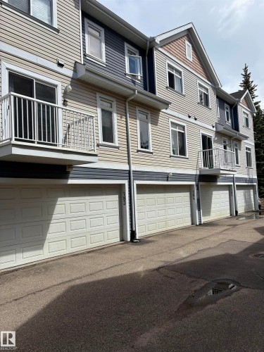 Multi-level exterior featuring light beige and dark blue horizontal siding, white trim, multiple balconies with white railings, and individual garage doors - 184 1804 70 Street, Edmonton, AB 