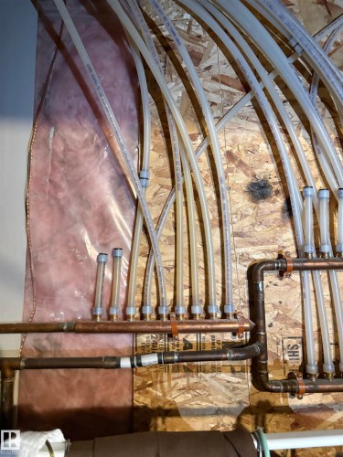 PEX tubing and copper piping system mounted on plywood sheathing, with visible insulation in the background - 184 1804 70 Street, Edmonton, AB 