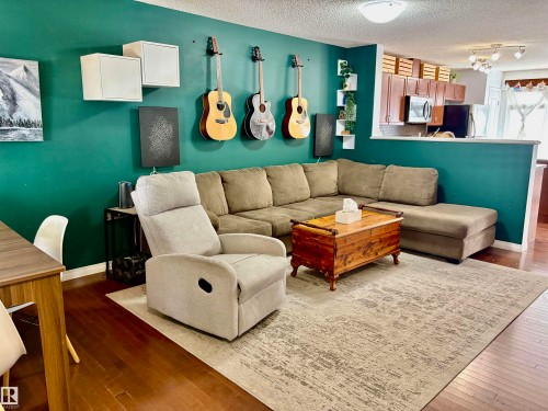 Open-concept living space featuring wood-finish flooring, a vibrant accent wall, and recessed lighting - 184 1804 70 Street, Edmonton, AB 