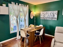 Dining area featuring deep green walls, a large window, rich wood-finish flooring, and white baseboards - 