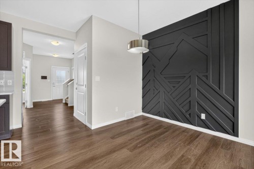 Dining area with a black accent wall featuring geometric paneling, wood-finish flooring, and a contemporary pendant light fixture - 2144 51 Street, Edmonton, AB 