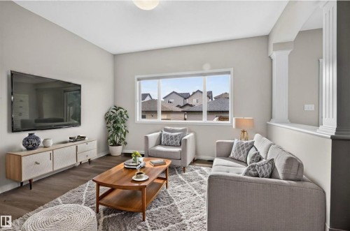 Bright living area featuring wood-finish flooring, a large window, light-toned wall paint, and decorative half-walls with columns - 2144 51 Street, Edmonton, AB 