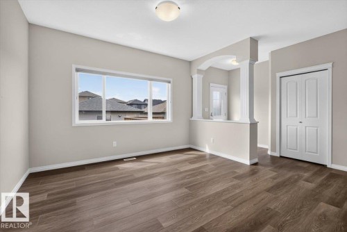 Open concept living area featuring wood-finish flooring, a large window, neutral wall tones, and decorative archways with columns - 2144 51 Street, Edmonton, AB 