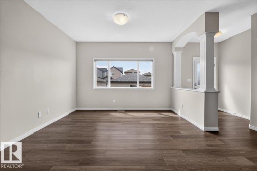 Spacious room featuring wood-finish flooring, neutral-toned walls, and a large window - 2144 51 Street, Edmonton, AB 