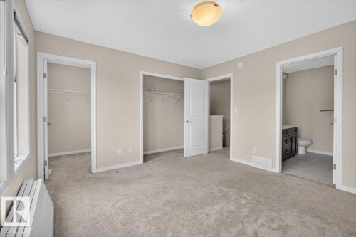 Carpeted bedroom featuring two closet spaces, a window with a radiator, and direct access to a bathroom with a dark wood vanity and tiled flooring - 2144 51 Street, Edmonton, AB 