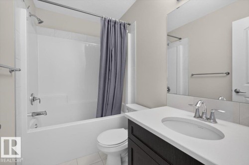 Bathroom featuring a white tub/shower combination with chrome fixtures, a dark wood-finish vanity with a white countertop and integrated sink, and a large wall-mounted mirror - 2144 51 Street, Edmonton, AB 