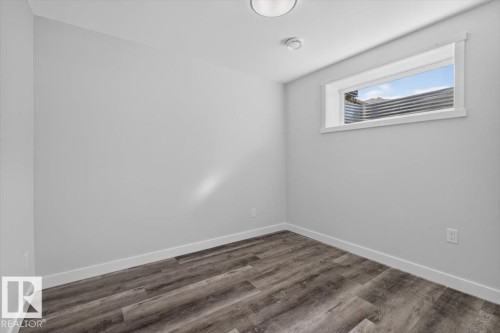 Room featuring neutral-toned walls, wood-finish flooring, white baseboards, and a window with a white frame - 2144 51 Street, Edmonton, AB 