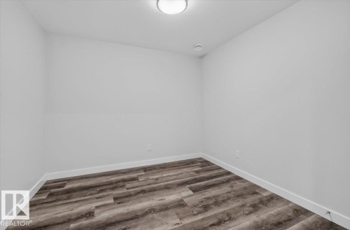 Neutral white walls featuring wood-finish flooring, white baseboards, and a flush-mount ceiling light - 2144 51 Street, Edmonton, AB 