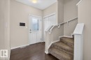 Inviting entryway featuring dark wood-finish flooring, a white front door with decorative glass, white trim, and a carpeted staircase with a white railing - 2144 51 Street, Edmonton, AB 