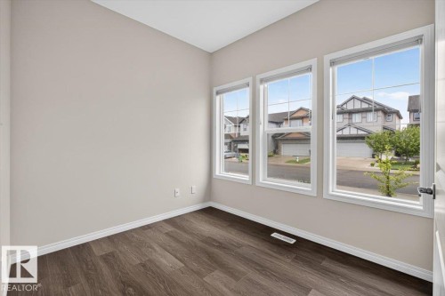 Room featuring three large windows with white trim, wood-finish flooring, and light neutral wall paint - 2144 51 Street, Edmonton, AB 