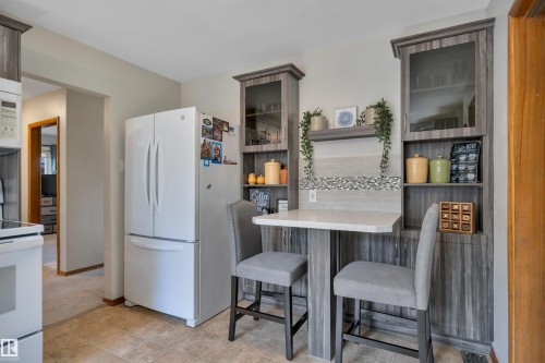 Kitchen area featuring custom cabinetry with glass-front uppers, a built-in dining counter with a light-colored solid surface, and a mosaic tile backsplash - 9835 74 Street, Edmonton, AB 
