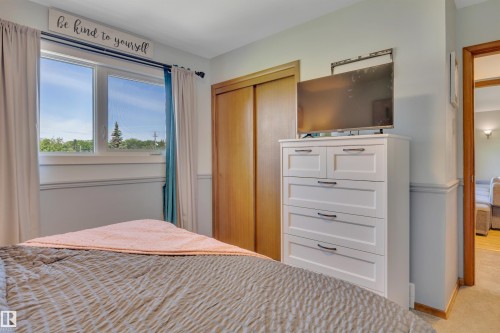 Bedroom featuring a dual-pane window, wood-finish closet doors, and light-toned walls with wainscoting - 9835 74 Street, Edmonton, AB 