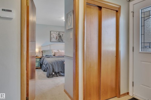 Carpeted bedroom with a light blue wall color and a tufted headboard, featuring wood-finish door frames and a bi-fold closet door - 9835 74 Street, Edmonton, AB 