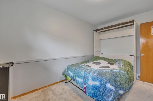 Recessed wall bed with integrated lighting, wood-finish door, light gray walls, white baseboard trim, and light-toned carpet flooring - 9835 74 Street, Edmonton, AB 