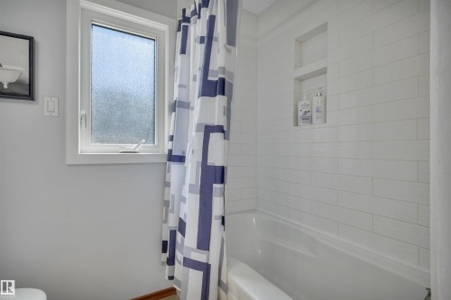 Bathtub with white subway tile surround, integrated shower niche, and a frosted window - 9835 74 Street, Edmonton, AB 