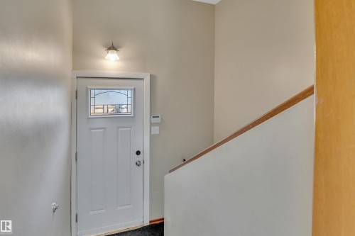 Entryway featuring a white paneled door with decorative glass, a wall-mounted light fixture, and a light-toned wood handrail - 9835 74 Street, Edmonton, AB 