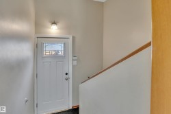 Entryway featuring a white paneled door with decorative glass, a wall-mounted light fixture, and a light-toned wood handrail - 