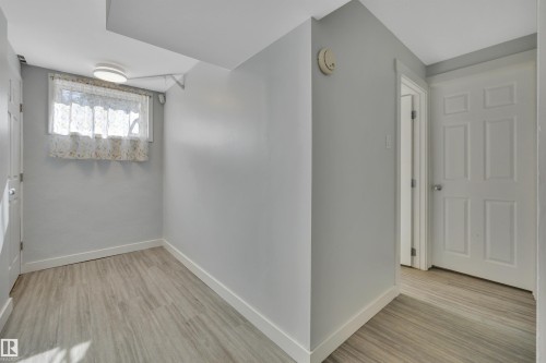 Hallway featuring light wood-finish flooring, light grey painted walls, white baseboards, and a white paneled door - 9835 74 Street, Edmonton, AB 