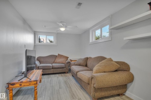 Finished lower level space featuring wood-finish flooring, light gray walls, a ceiling fan, two windows, and two wall-mounted shelves - 9835 74 Street, Edmonton, AB 