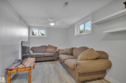 Finished lower level space featuring wood-finish flooring, light gray walls, a ceiling fan, two windows, and two wall-mounted shelves - 