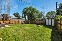Expansive backyard featuring a manicured lawn, full wood fencing, a dedicated fire pit area, a white storage shed, and a concrete patio pad - 