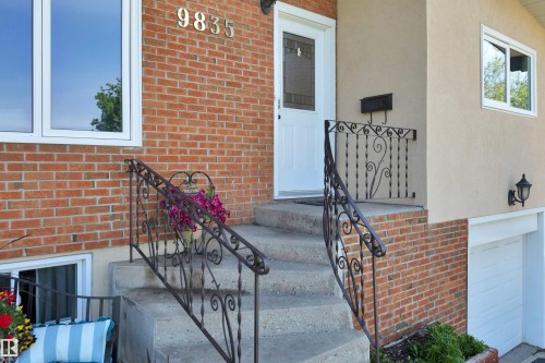Front entrance featuring concrete steps with decorative wrought iron railings, brick facade, stucco siding, and a white entry door with a privacy screen insert - 9835 74 Street, Edmonton, AB 