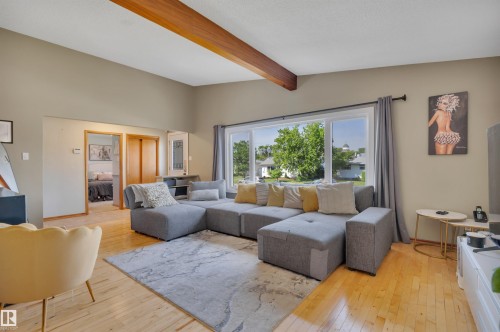 Spacious living area featuring exposed wood ceiling beams, wood-finish flooring, and a large window - 9835 74 Street, Edmonton, AB 