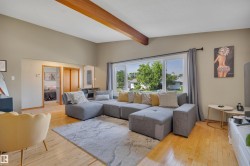 Spacious living area featuring exposed wood ceiling beams, wood-finish flooring, and a large window - 
