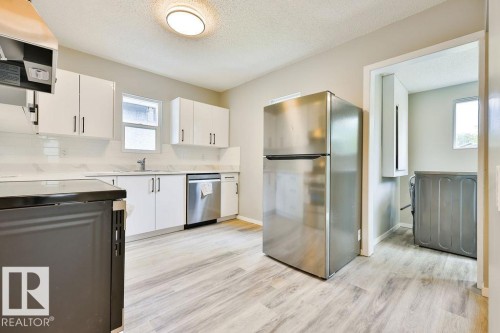 Modern kitchen featuring wood-finish flooring, white cabinetry with dark pulls, stainless steel appliances, and a light-toned backsplash - 11241 88 Street, Edmonton, AB 