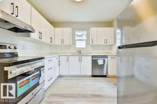 Bright kitchen featuring white cabinetry with black hardware, stainless steel appliances, light countertops, a white subway tile backsplash, and wood-finish flooring - 11241 88 Street, Edmonton, AB 
