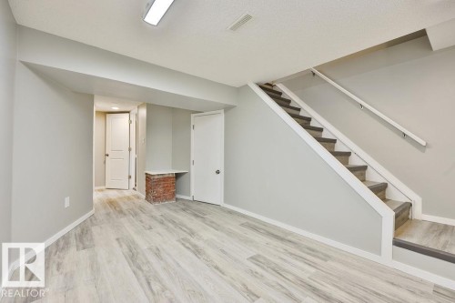 Finished lower level with light wood-finish flooring, light gray wall paint, white trim, and a carpeted staircase with white handrails - 11241 88 Street, Edmonton, AB 