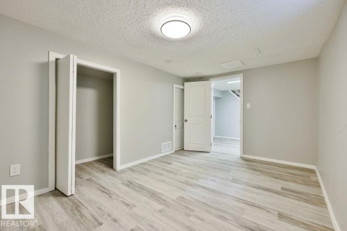 Spacious room featuring light wood-finish flooring, neutral gray walls, white baseboards, and a flush-mount ceiling light fixture - 11241 88 Street, Edmonton, AB 