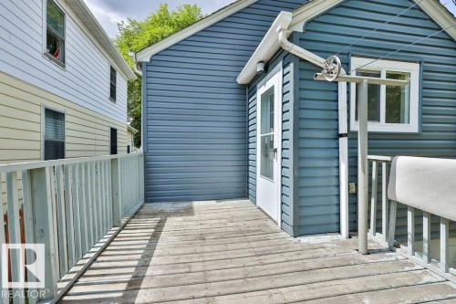 Exterior deck with wood decking and white railing, featuring a blue vinyl-sided structure with a white entry door and a white-framed window - 11241 88 Street, Edmonton, AB 