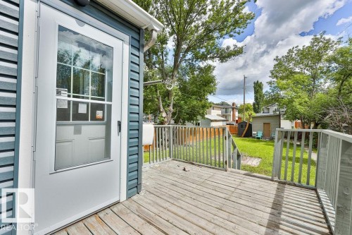 Rear exterior featuring horizontal siding in a blue hue, a white storm door, and a wooden deck with railing - 11241 88 Street, Edmonton, AB 