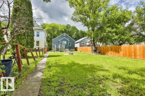 Expansive grassy yard featuring a concrete pathway, a newly installed wood fence, mature trees, and a fire pit area - 11241 88 Street, Edmonton, AB 