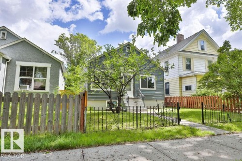 Front exterior featuring horizontal siding, a wrought iron fence, a concrete walkway, mature trees, and an established lawn - 11241 88 Street, Edmonton, AB 