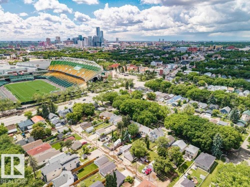 Aerial perspective showcasing residential properties with mature trees, a stadium featuring green and yellow seating, and a distant city skyline with high-rise buildings - 11241 88 Street, Edmonton, AB 