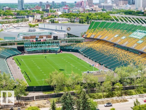 Sports stadium featuring a green playing field with white markings, surrounded by tiered seating in green and yellow - 11241 88 Street, Edmonton, AB 