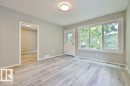 Bright room featuring light wood-finish flooring, a white paneled entry door with decorative glass, and a large triple window with white trim - 11241 88 Street, Edmonton, AB 
