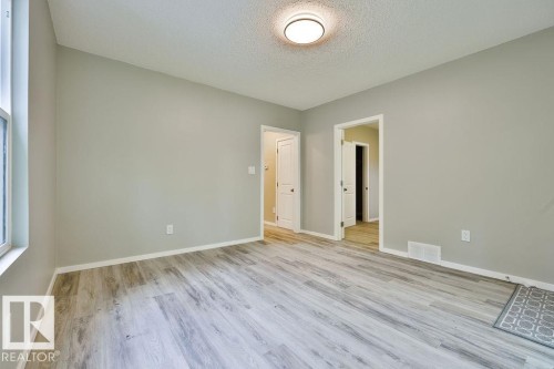 Spacious room featuring light wood-finish flooring, neutral gray wall paint, and white trim - 11241 88 Street, Edmonton, AB 