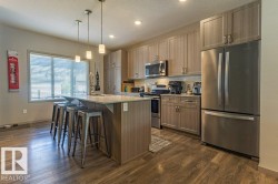 Contemporary kitchen featuring an island with pendant lighting, stainless steel appliances, wood-finish flooring, ample cabinetry, and a window with blinds - 