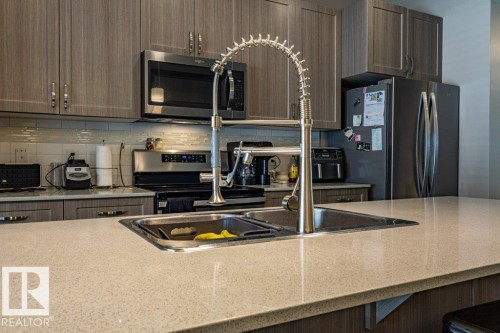 Kitchen featuring a dual-basin stainless steel sink with a high-arc pull-down faucet, light-toned speckled countertops, and wood-finish cabinetry - 17123 49 Street, Edmonton, AB 