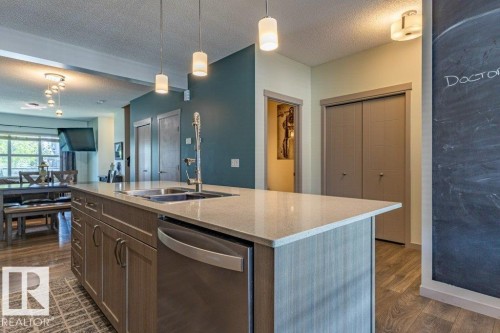 Kitchen island featuring a double-basin stainless steel sink, pull-down faucet, and integrated dishwasher - 17123 49 Street, Edmonton, AB 