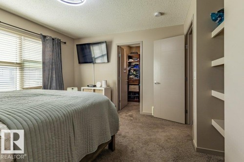 Carpeted interior space featuring a window with horizontal blinds and a privacy curtain, a built-in closet with shelving, a modern ceiling light fixture, and wall-mounted shelving - 17123 49 Street, Edmonton, AB 