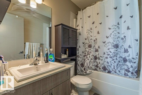 Bathroom featuring a built-in vanity with an integrated sink, a large wall-mounted mirror, a tub-shower combination, and a wall-mounted storage cabinet - 17123 49 Street, Edmonton, AB 